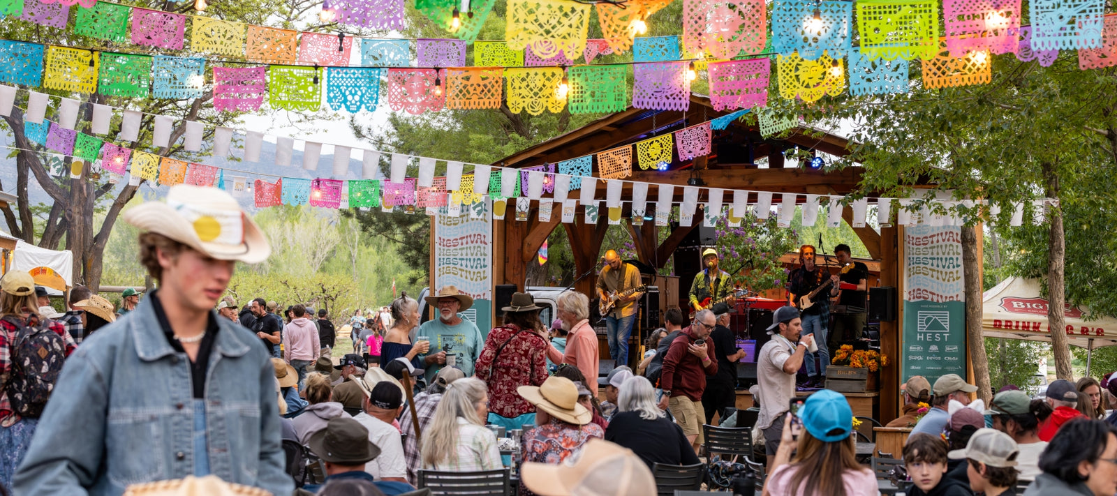 Festival camping scene at HESTIVAL 2026 in Colorado featuring colorful flags, campers gathered outdoors, live music atmosphere, and community celebrating public lands at Big B’s Delicious Orchards